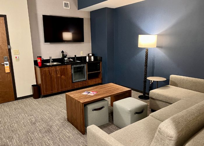 Living area in Drury Inn suite, showcasing a plush sectional and an equipped wet bar with a mini-fridge.